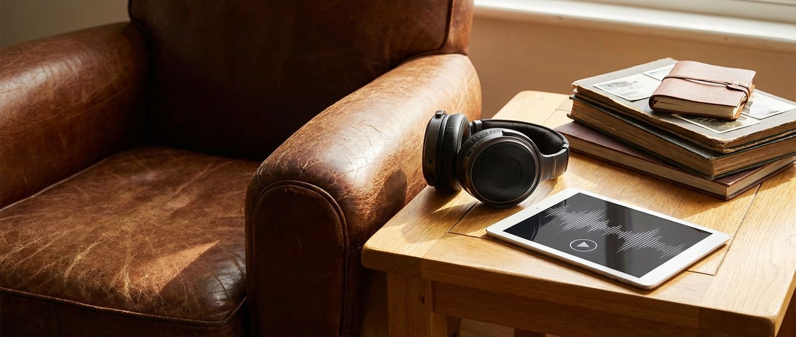 Headphones and a tablet displaying an audio waveform on a side table next to a leather armchair